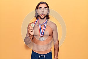 Young handsome man wearing swimwear and medals scared and amazed with open mouth for surprise, disbelief face