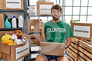 Young handsome man wearing volunteer t shirt using laptop pointing aside worried and nervous with forefinger, concerned and