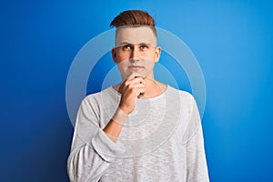Young handsome man wearing white casual t-shirt standing over isolated blue background serious face thinking about question, very