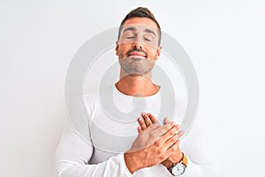 Young handsome man wearing white shirt over isolated background smiling with hands on chest with closed eyes and grateful gesture