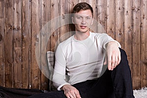 Young handsome man wearing white sweater sitting near wood wall