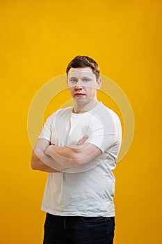 Young handsome man wearing white t-shirt with crossed arms looking at the camera over yellow studio background