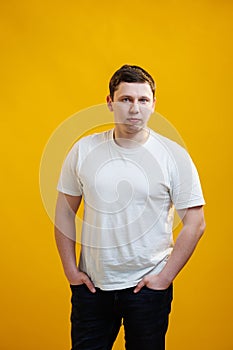 Young handsome man wearing white t-shirt with focused face looking at the camera over yellow studio background