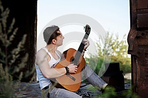 Young handsome man, wearing white t-shirt and grey pants, sitting inside old railway carriage, playing guitar, composing music