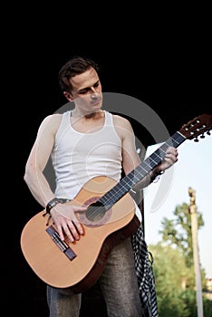 Young handsome man, wearing white t-shirt and grey pants, standing inside old railway carriage, playing guitar, composing music