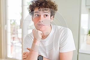 Young handsome man wearing white t-shirt with hand on chin thinking about question, pensive expression