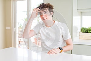 Young handsome man wearing white t-shirt at home very happy and smiling looking far away with hand over head