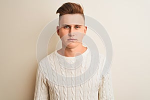 Young handsome man wearing winter sweater standing over isolated white background with serious expression on face