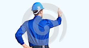 Young handsome man wearing worker uniform and hardhat backwards thinking about doubt with hand on head