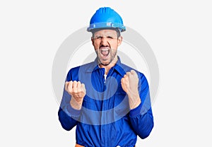 Young handsome man wearing worker uniform and hardhat celebrating surprised and amazed for success with arms raised and eyes