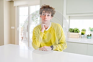 Young handsome man wearing yellow sweater at home with hand on chin thinking about question, pensive expression