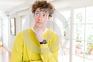 Young handsome man wearing yellow sweater at home with hand on chin thinking about question, pensive expression