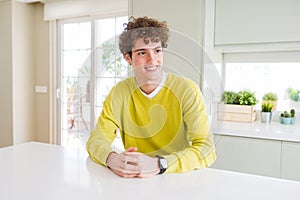 Young handsome man wearing yellow sweater at home looking away to side with smile on face, natural expression