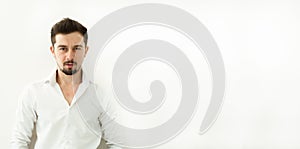 Young handsome man in white blouse stand on white background. Horizontal shot of serious stylish confident in white shirt man with