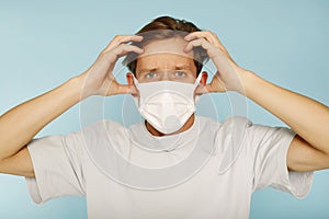 Young handsome man in white health care face mask standing with hand on head over blue background