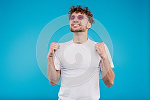Young handsome man in white shirt stands in winning position, self-defense concept, boxing, on isolated blue background