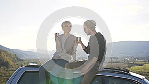 Young handsome man and woman drinking tea, relaxing on the mountain background.