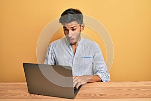 Young handsome man working at the office with laptop scared and amazed with open mouth for surprise, disbelief face