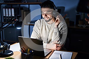 Young handsome man working using computer laptop at night with a big smile on face, pointing with hand and finger to the side