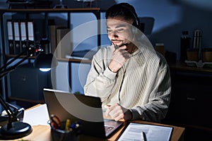 Young handsome man working using computer laptop at night looking confident at the camera with smile with crossed arms and hand