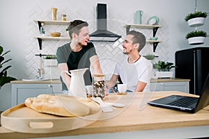 Young handsome men sitting in the kitchen and having breakfast and coffee together.