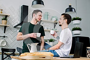 Young handsome men sitting in the kitchen and having breakfast and coffee together.