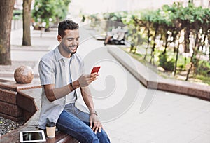 Young handsome men using smartphone in a city. Smiling student man texting on his mobile phone. Coffee break.