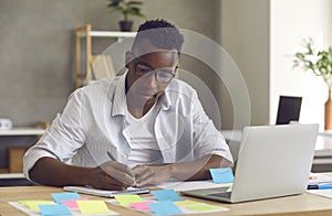 Young handsome minded black businessman writing down ideas in notebook