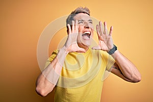 Young handsome modern man wearing yellow shirt over yellow isolated background Shouting angry out loud with hands over mouth