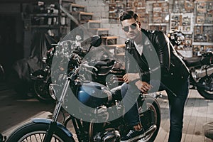 young handsome motorcyclist in black leather jacket with classic motorbikes