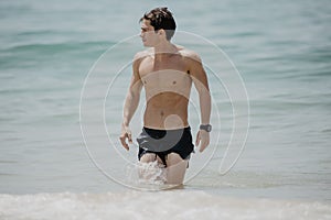 Young handsome muscular man walking out of the water in a tropical beach wearing a bathing suit