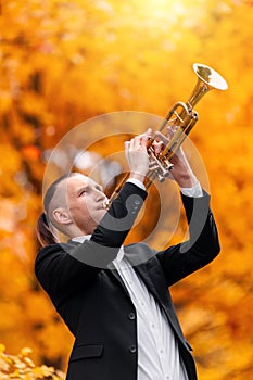 Young handsome musican plays golden trumpet in autumn park