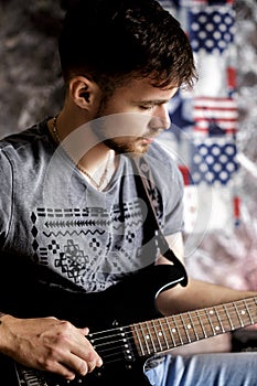 Young handsome musician playing electric guitar on dark background