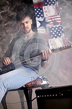 Young handsome musician playing electric guitar on dark background