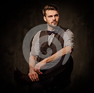 Young handsome old-fashioned man with beard posing on dark background.