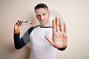 Young handsome optical man showing glasses standing over isolated white background with open hand doing stop sign with serious and