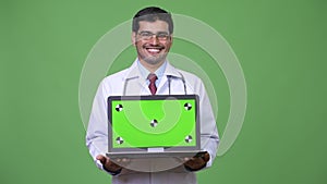 Young handsome Persian man doctor showing laptop