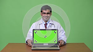Young handsome Persian man doctor showing laptop