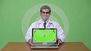 Young handsome Persian man doctor showing laptop