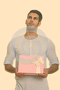 Young handsome Persian man holding gift box while thinking