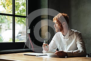 Young handsome readhead bearded man sitting on the workplace at