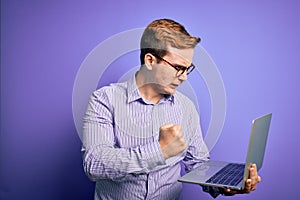 Young handsome redhead businessman working using laptop over purple background annoyed and frustrated shouting with anger, crazy