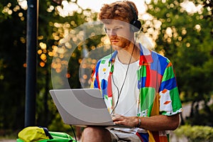 Young handsome redhead calm man in headphones working with laptop