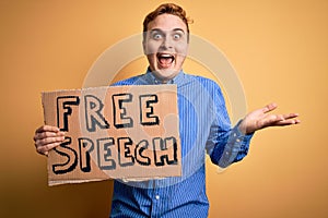 Young handsome redhead man asking for freedom holding banner with free speech message celebrating victory with happy smile and