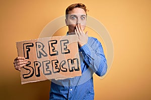 Young handsome redhead man asking for freedom holding banner with free speech message covering mouth with hand, shocked and afraid