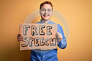 Young handsome redhead man asking for freedom holding banner with free speech message looking positive and happy standing and