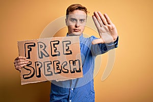 Young handsome redhead man asking for freedom holding banner with free speech message with open hand doing stop sign with serious