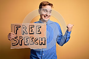 Young handsome redhead man asking for freedom holding banner with free speech message pointing thumb up to the side smiling happy