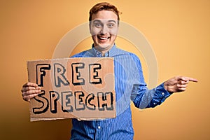 Young handsome redhead man asking for freedom holding banner with free speech message Smiling happy pointing with hand and finger