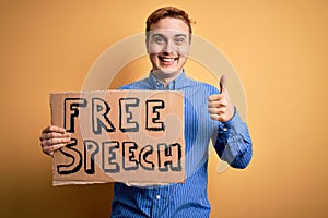 Young handsome redhead man asking for freedom holding banner with free speech message Smiling happy and positive, thumb up doing